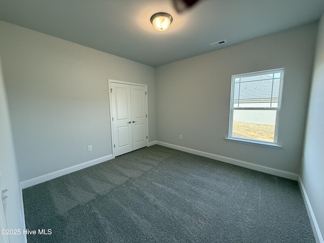 spare room with visible vents, dark carpet, and baseboards