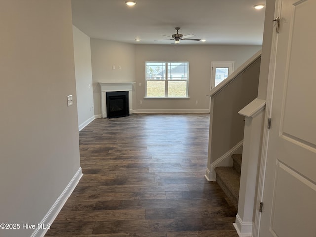 unfurnished living room with ceiling fan, dark wood-style flooring, a fireplace, baseboards, and stairs