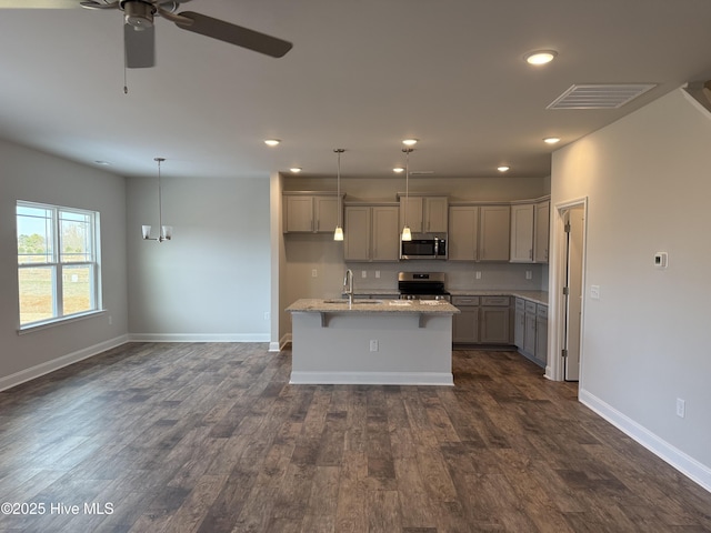 kitchen with gray cabinetry, hanging light fixtures, appliances with stainless steel finishes, light stone countertops, and an island with sink