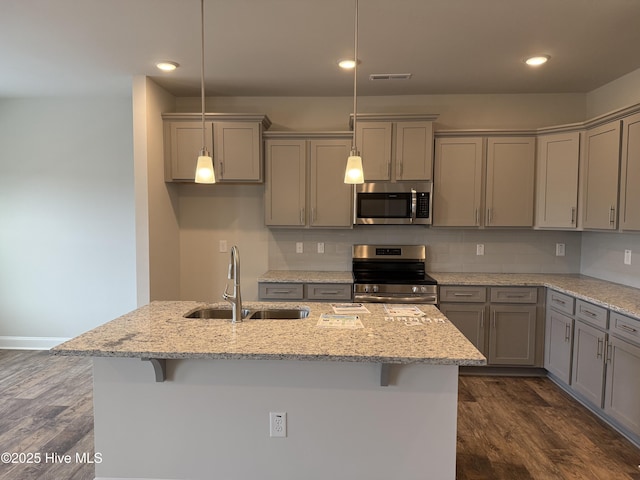 kitchen featuring light stone countertops, stainless steel appliances, a sink, and decorative light fixtures