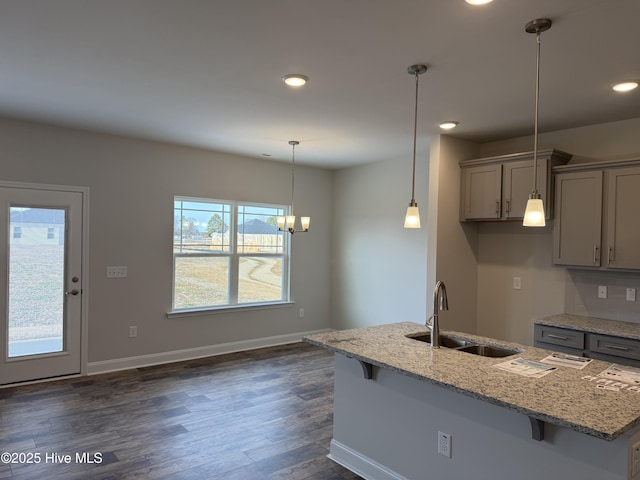 kitchen featuring light stone counters, dark wood-style floors, decorative light fixtures, a sink, and baseboards