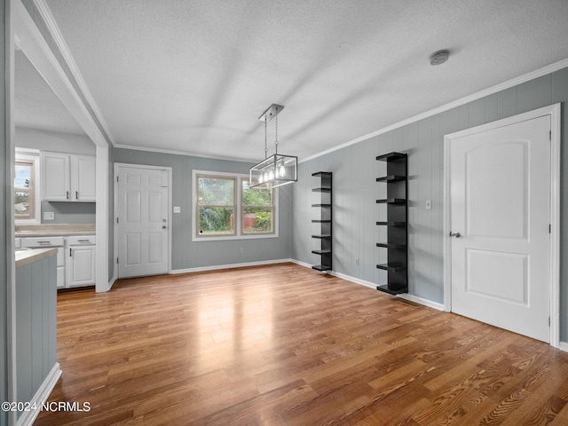 unfurnished dining area featuring crown molding, a notable chandelier, light hardwood / wood-style flooring, and a textured ceiling