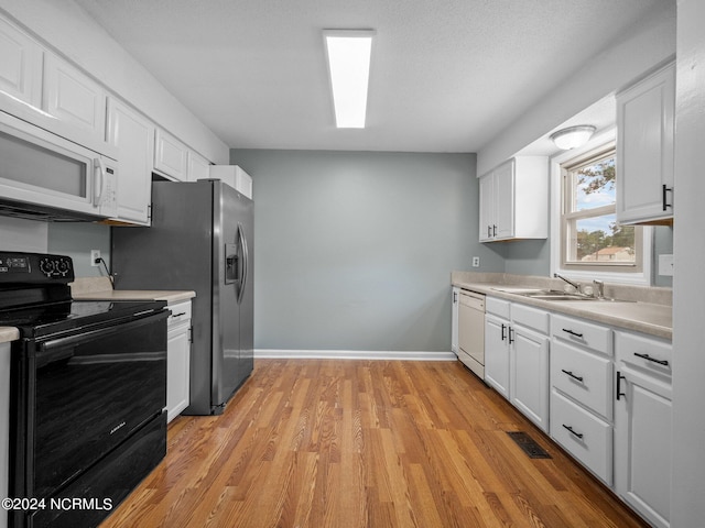 kitchen featuring white appliances, white cabinets, light countertops, light wood-type flooring, and a sink