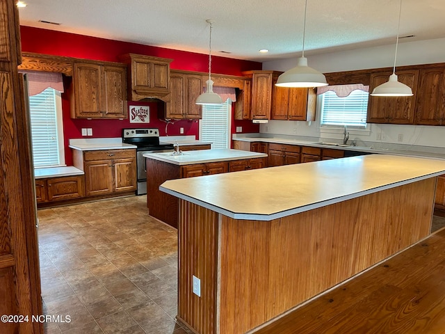 kitchen with decorative light fixtures, stainless steel range with electric cooktop, sink, dark tile patterned flooring, and a kitchen island with sink