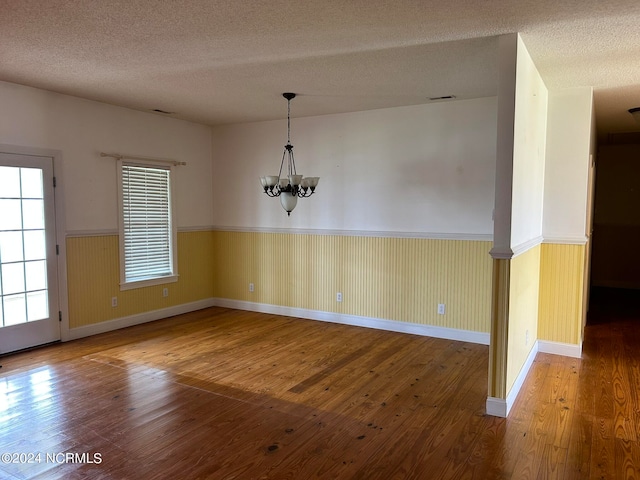 unfurnished dining area with wood-type flooring, a notable chandelier, and a textured ceiling