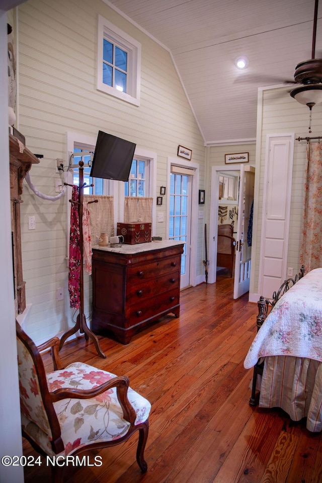 bedroom featuring lofted ceiling, hardwood / wood-style flooring, wood walls, and ornamental molding