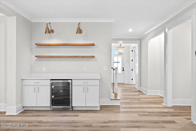 bar with ornamental molding, beverage cooler, light wood-type flooring, and white cabinets