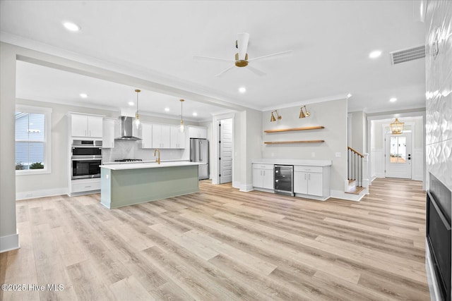 kitchen featuring decorative light fixtures, wine cooler, white cabinets, a center island with sink, and wall chimney exhaust hood