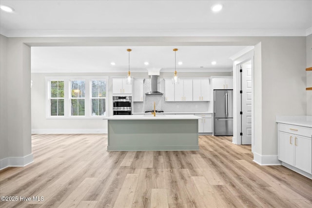 kitchen with stainless steel appliances, hanging light fixtures, wall chimney range hood, and a center island with sink