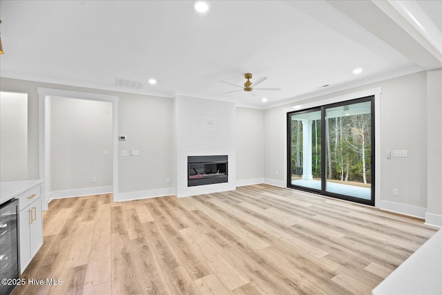 unfurnished living room featuring a large fireplace, beverage cooler, ornamental molding, ceiling fan, and light hardwood / wood-style floors