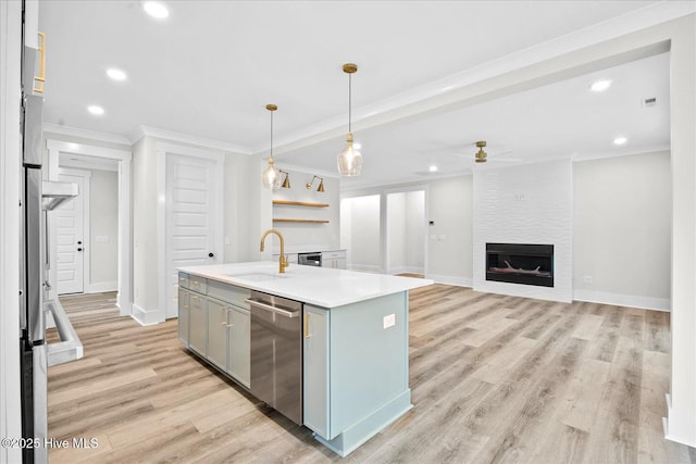 kitchen with sink, a kitchen island with sink, ornamental molding, a large fireplace, and stainless steel dishwasher