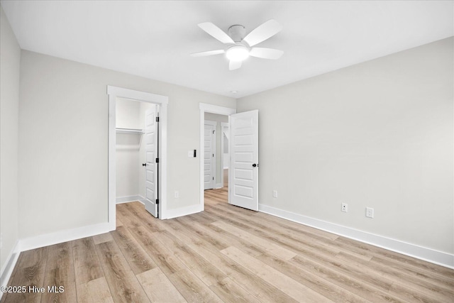 unfurnished bedroom featuring a spacious closet, a closet, ceiling fan, and light wood-type flooring