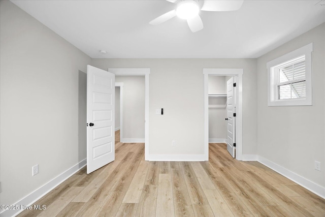 unfurnished bedroom with ceiling fan, a walk in closet, a closet, and light wood-type flooring