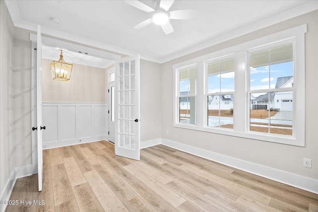 spare room featuring crown molding, ceiling fan with notable chandelier, light wood-type flooring, and french doors