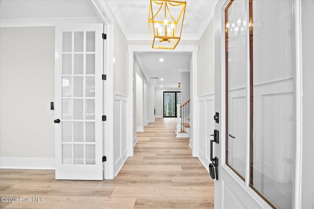 hall with an inviting chandelier, ornamental molding, and light hardwood / wood-style floors