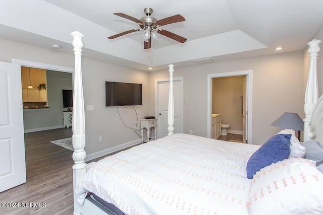 bedroom with hardwood / wood-style flooring, ensuite bathroom, ceiling fan, and a raised ceiling