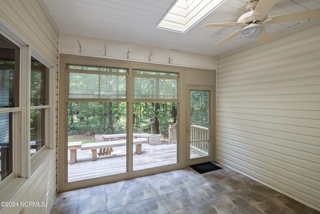 doorway to outside featuring ceiling fan, a skylight, and wooden walls