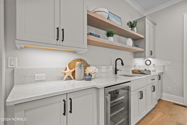 kitchen featuring light stone countertops, sink, wine cooler, light hardwood / wood-style flooring, and white cabinets