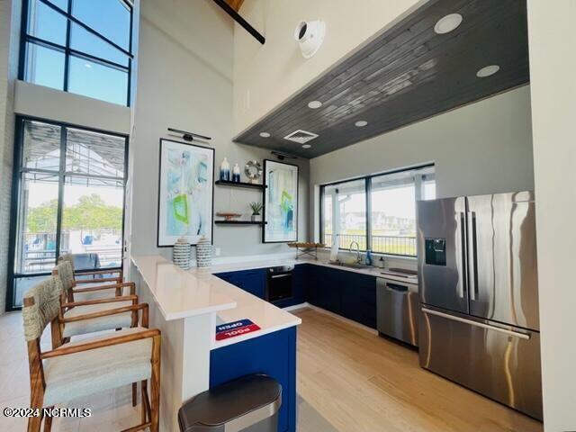 kitchen featuring stainless steel appliances, light hardwood / wood-style floors, sink, kitchen peninsula, and blue cabinets