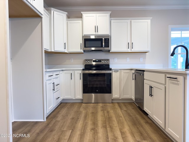 kitchen featuring light wood-type flooring, appliances with stainless steel finishes, white cabinetry, and ornamental molding