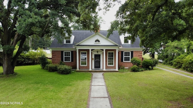 greek revival inspired property with brick siding, a front yard, and a porch