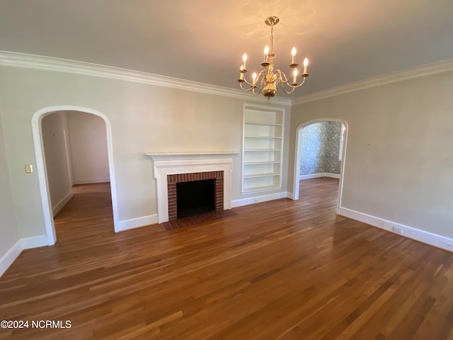 unfurnished living room with dark hardwood / wood-style flooring, a brick fireplace, crown molding, built in features, and a notable chandelier