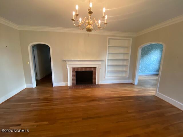 unfurnished living room with ornamental molding, a brick fireplace, a chandelier, and dark hardwood / wood-style floors