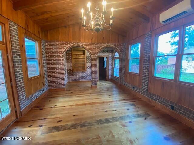 interior space featuring vaulted ceiling with beams, an AC wall unit, brick wall, hardwood / wood-style floors, and a chandelier