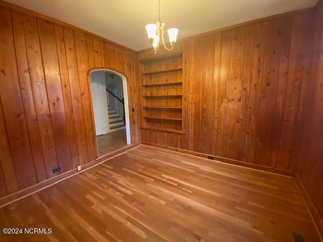 spare room with wood walls, a chandelier, wood-type flooring, and built in shelves