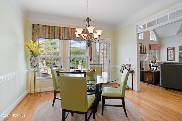 dining space featuring light wood-type flooring, a fireplace, crown molding, and an inviting chandelier