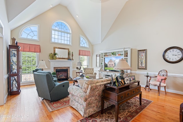 living area with high vaulted ceiling, a glass covered fireplace, light wood-style flooring, and baseboards