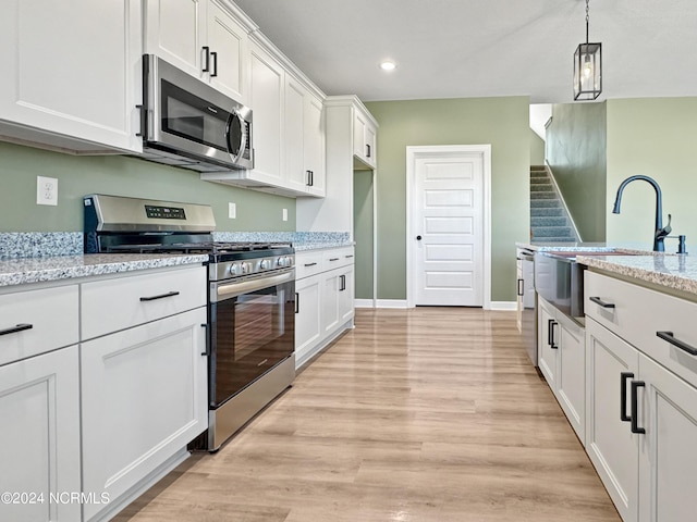 kitchen featuring stainless steel appliances, a sink, white cabinetry, hanging light fixtures, and light wood-type flooring