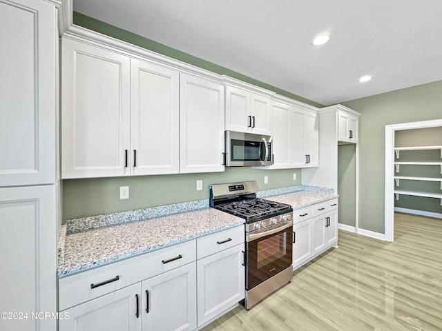 kitchen featuring light hardwood / wood-style floors, appliances with stainless steel finishes, white cabinetry, and light stone countertops