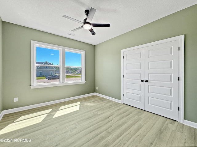 unfurnished bedroom with a closet, visible vents, a textured ceiling, wood finished floors, and baseboards