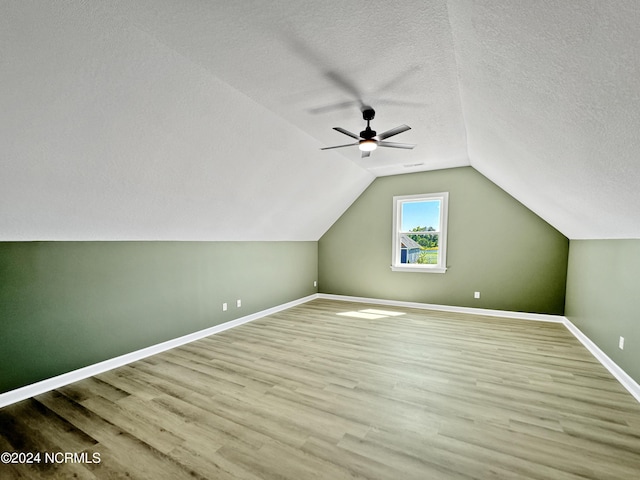 bonus room with a textured ceiling, lofted ceiling, wood finished floors, a ceiling fan, and baseboards