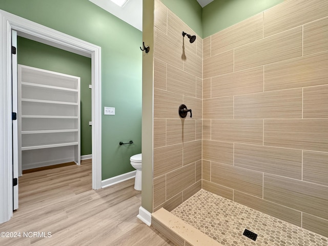 bathroom with toilet, wood finished floors, baseboards, tiled shower, and a walk in closet