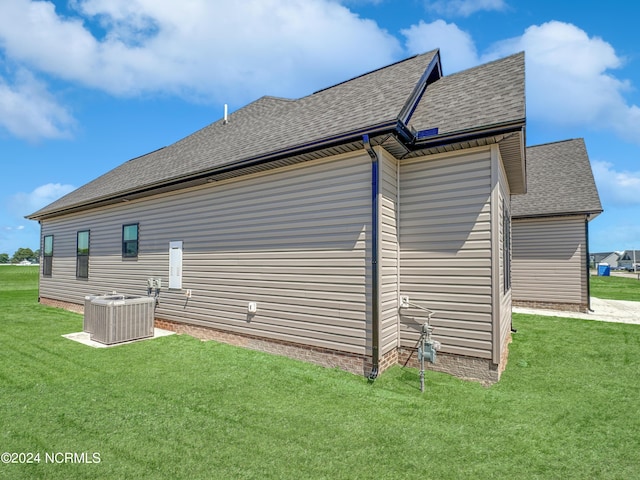 view of side of home with a shingled roof, cooling unit, and a lawn