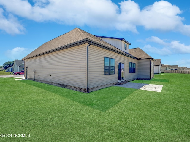 back of property with a yard, roof with shingles, and a patio area