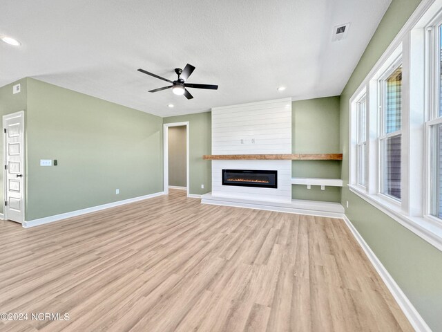 unfurnished living room featuring ceiling fan, a textured ceiling, light wood-type flooring, and a large fireplace