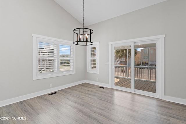 unfurnished dining area featuring hardwood / wood-style flooring, high vaulted ceiling, and a chandelier