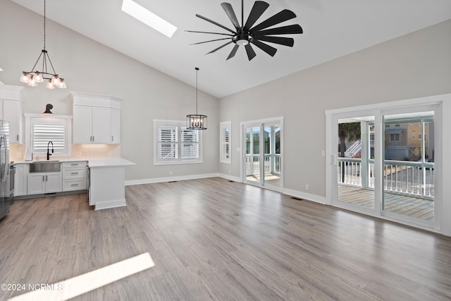 kitchen featuring a skylight, sink, backsplash, decorative light fixtures, and white cabinets