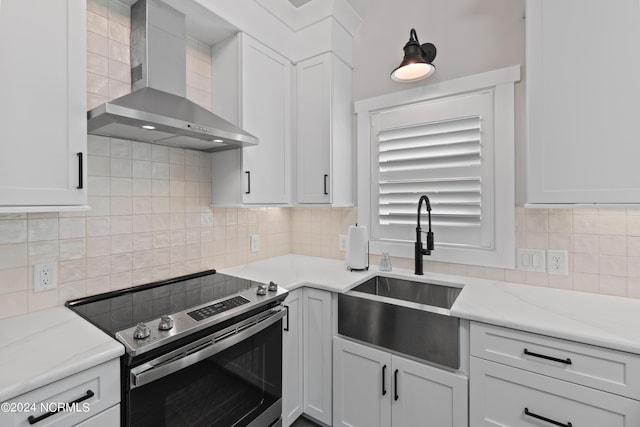 kitchen featuring wall chimney exhaust hood, stainless steel electric range, white cabinetry, and backsplash