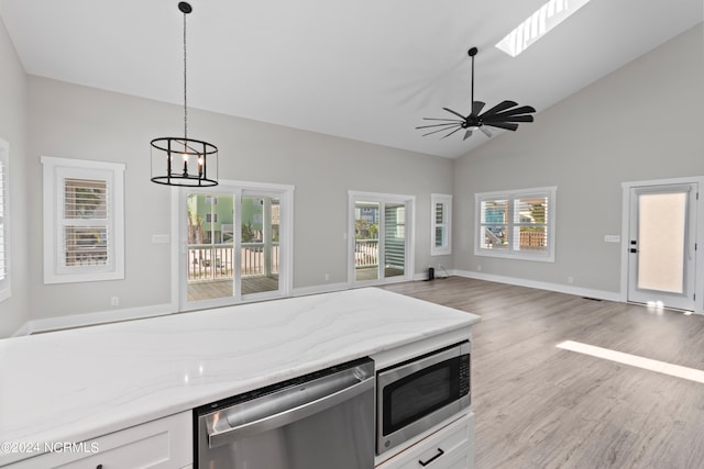 kitchen with a skylight, ceiling fan with notable chandelier, stainless steel appliances, pendant lighting, and white cabinets