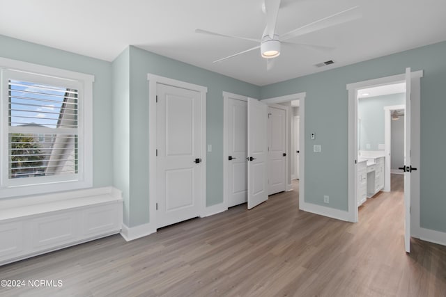 unfurnished bedroom with ceiling fan, ensuite bathroom, two closets, and light wood-type flooring