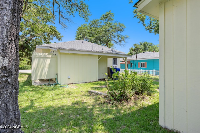 back of house with a shingled roof, a lawn, and fence