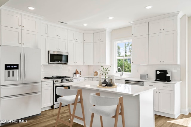 kitchen featuring stainless steel appliances, a center island, light hardwood / wood-style flooring, white cabinets, and a breakfast bar area