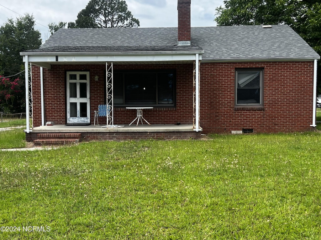 back of property featuring covered porch and a yard