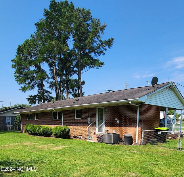 back of property with central air condition unit, fence, a lawn, and brick siding