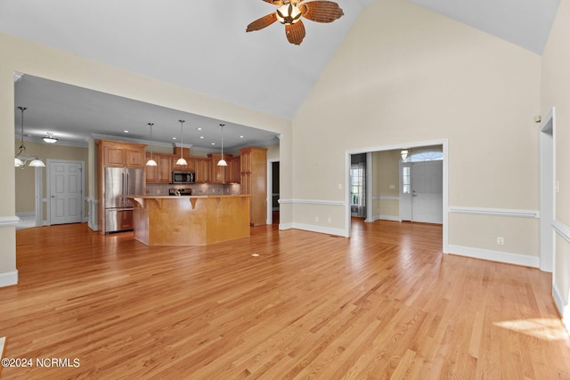 unfurnished living room with ceiling fan with notable chandelier, high vaulted ceiling, light wood finished floors, and baseboards