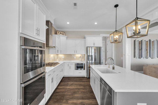 kitchen with wall chimney exhaust hood, appliances with stainless steel finishes, white cabinets, pendant lighting, and backsplash